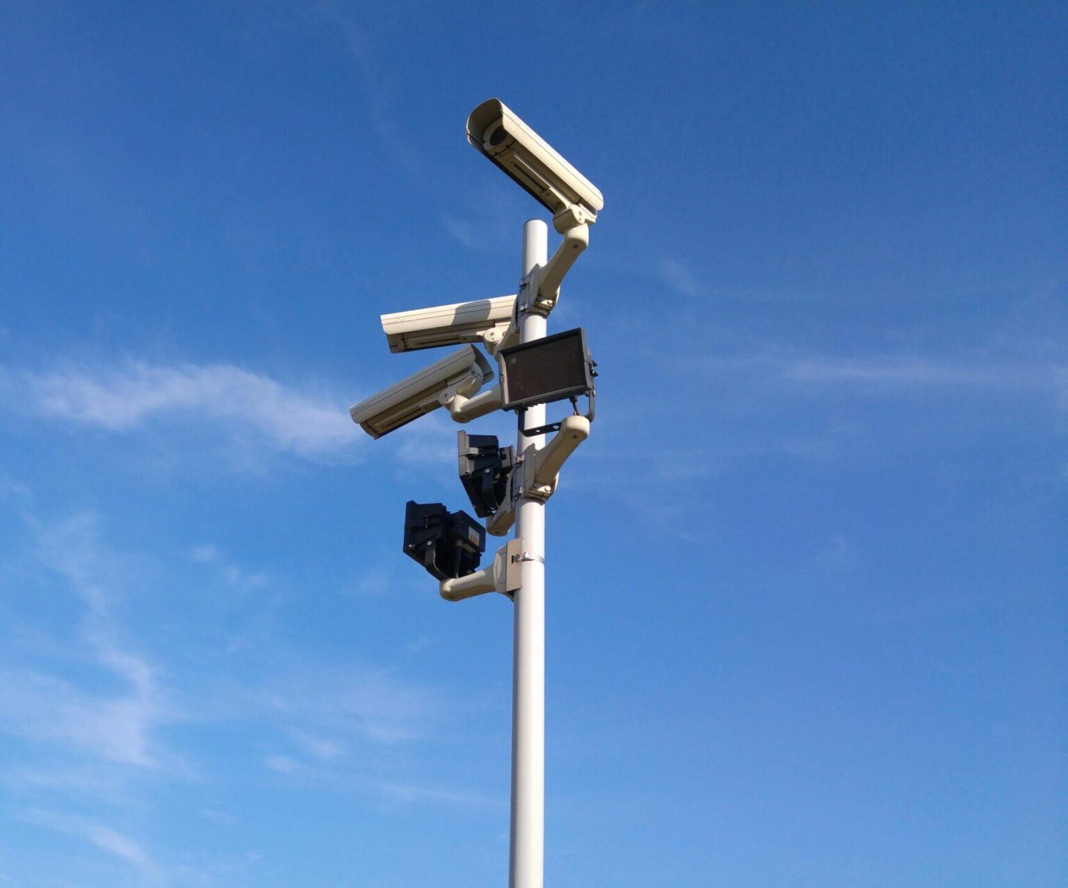 Multiple security cameras on a pole with a clear blue sky backdrop.